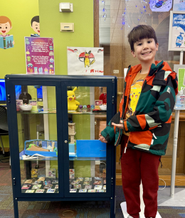 Young boy standing next to glass case filled with Pokemon cards