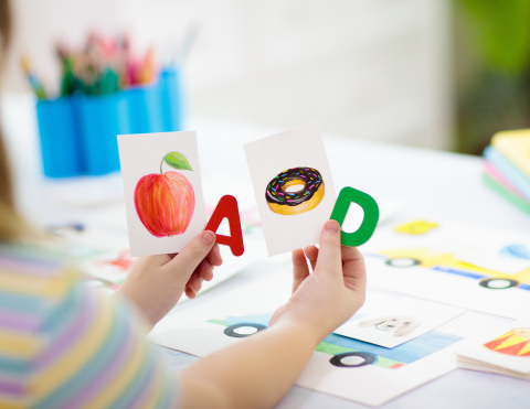 Photo of a child's hands holding cards with letters and pictures of food.