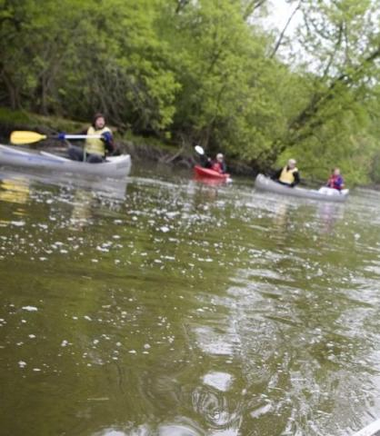 Photo of river with trees in the background and kayaks with people.