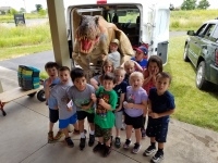 A group of children standing in front of a T-Rex figure.