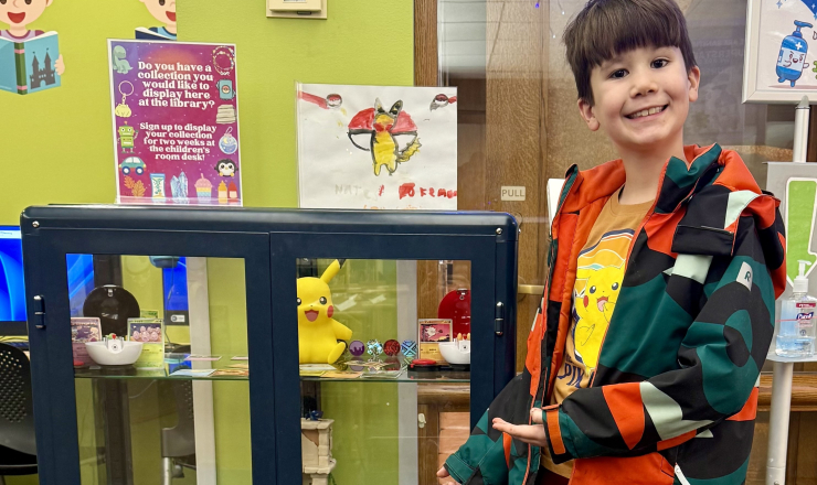 Young boy standing next to glass case filled with Pokemon cards